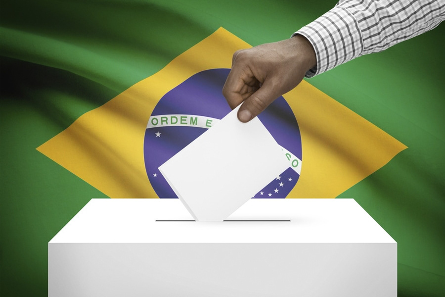 hand placing ballot in ballot box with brazil flag in background